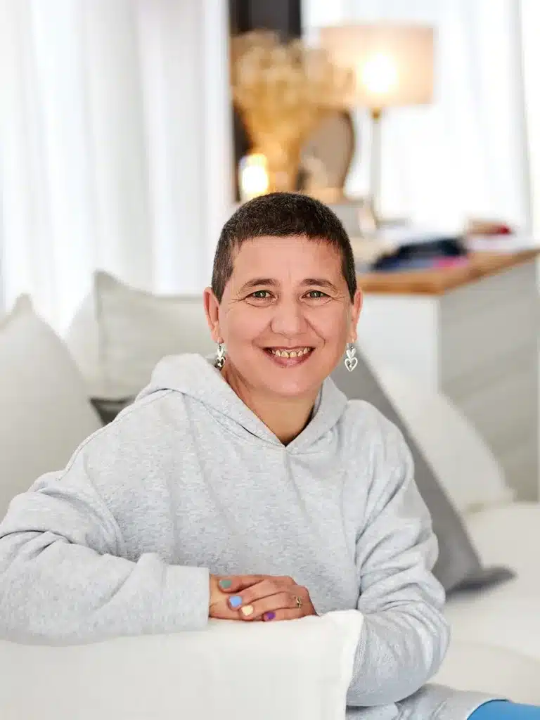Anaís Isarre - despierta tu alegría (mentora) Anaís Isarre sentada en un sofá mirando a cámara y sonriendo, mentora experta en recuperar la alegría de vivir.