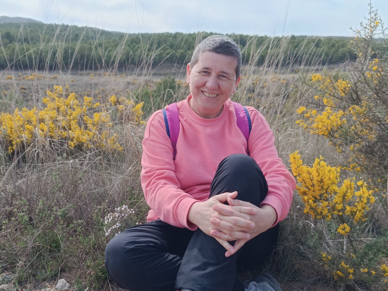 Anaís Isarre sentada sonriente en un campo de flores silvestres celebrando el inicio de la primavera y el Día de la Felicidad en su ruta por el río Aguasvivas.