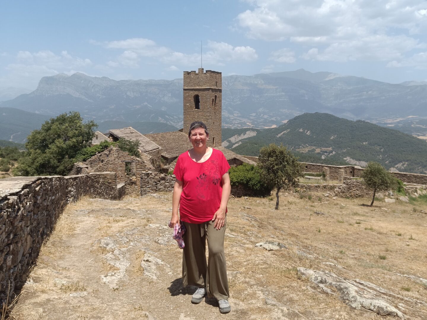 Anaís Isarre sonriendo delante de la torre medieval del Muro de Roda con el paisaje montañoso del Sobrarbe al fondo.