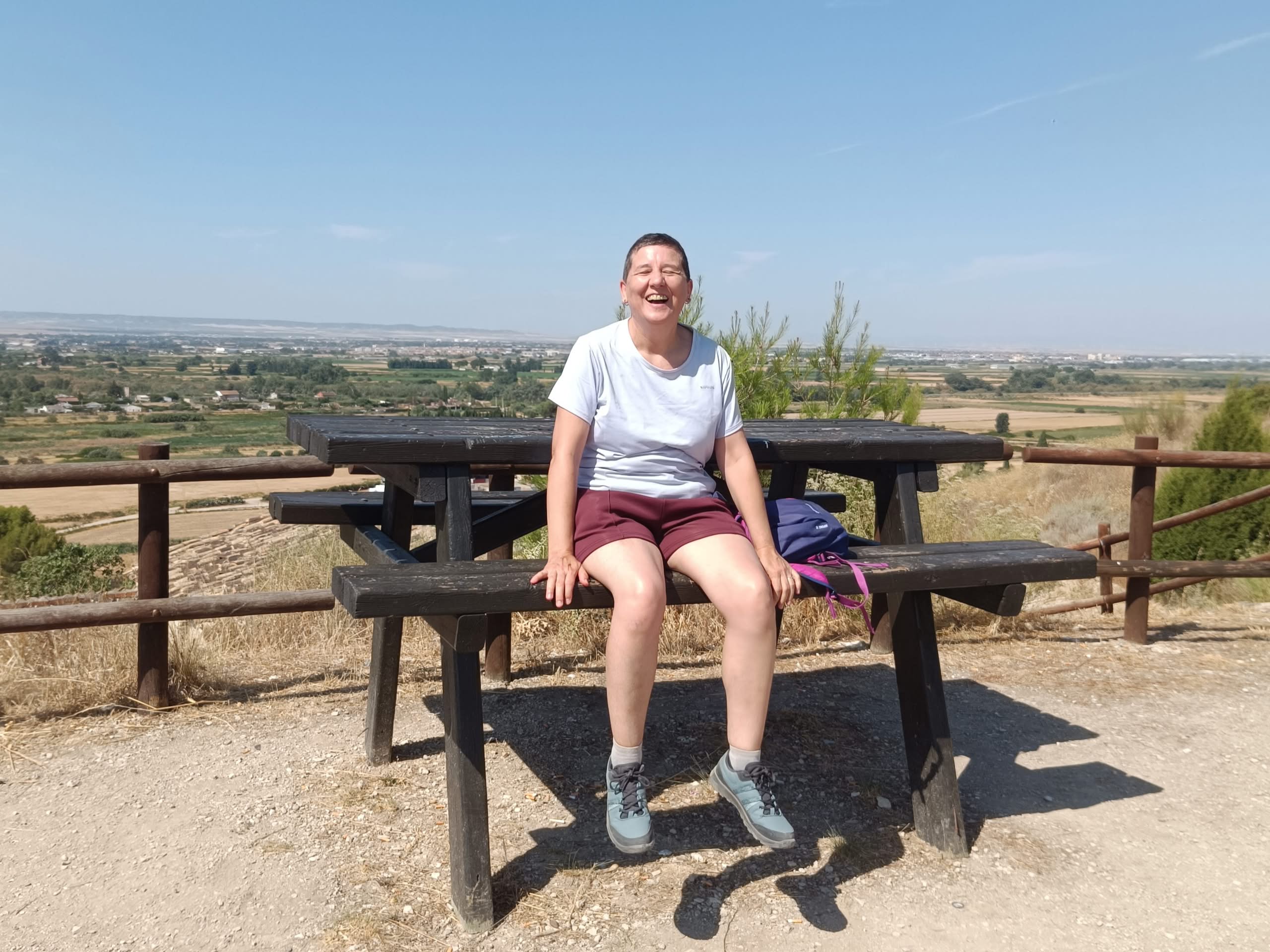 Anaís Isarre sentada en el banco de una mesa en el mirador de Alfocea y riendo porque está muy alto y los pies cuelgan.
