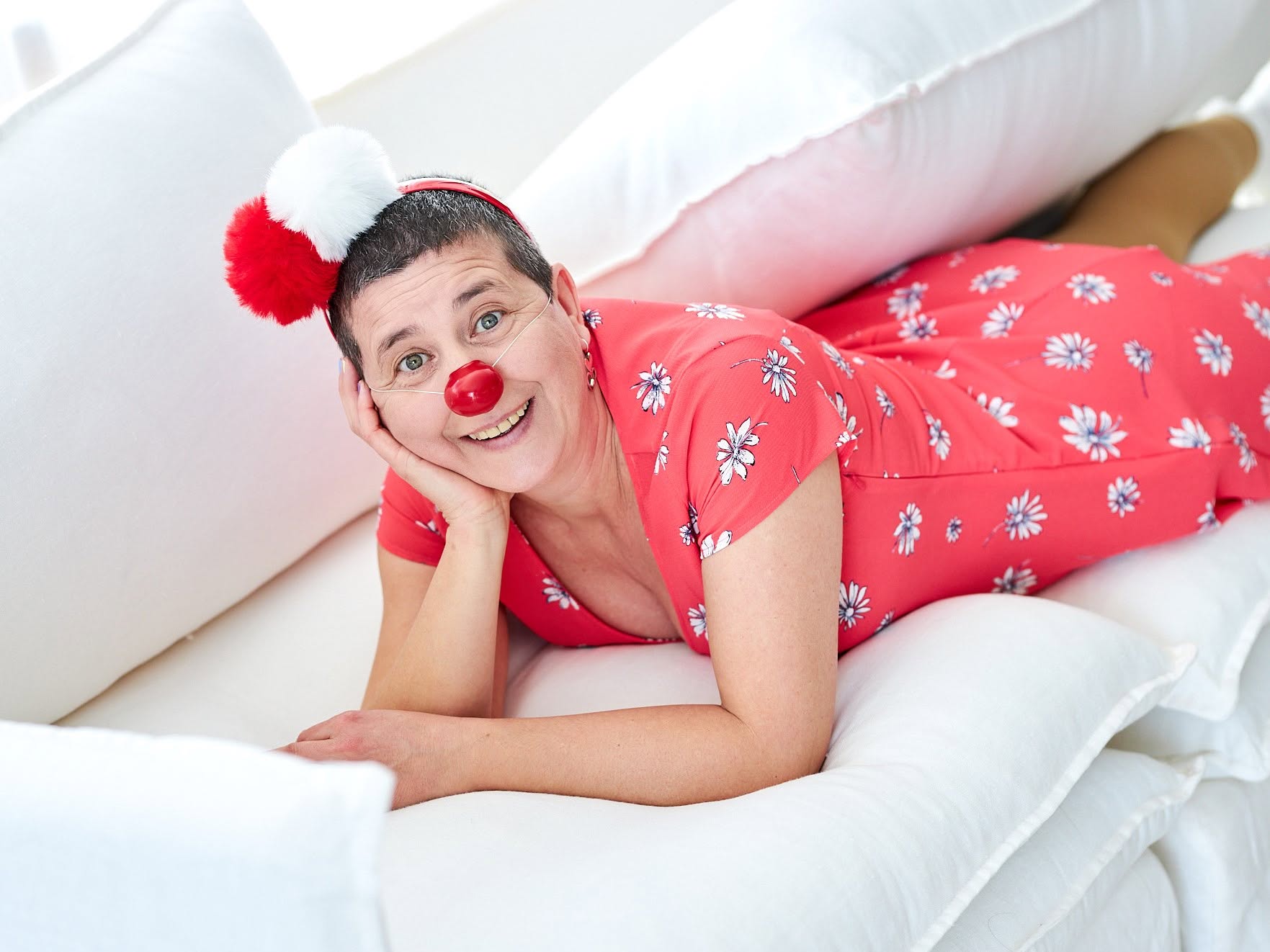 Pirueta, la payasa interior de Anaís Isarre sonriendo con su nariz roja de payasa recostada en un sofá blanco, representando el método Clown para la Vida.