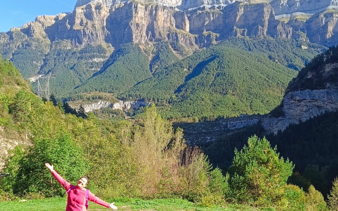 Anaís Isarre feliz con los brazos abiertos celebrando la llegada a los paisajes del Pirineo con los paredones rocosos de Ordesa de fondo.