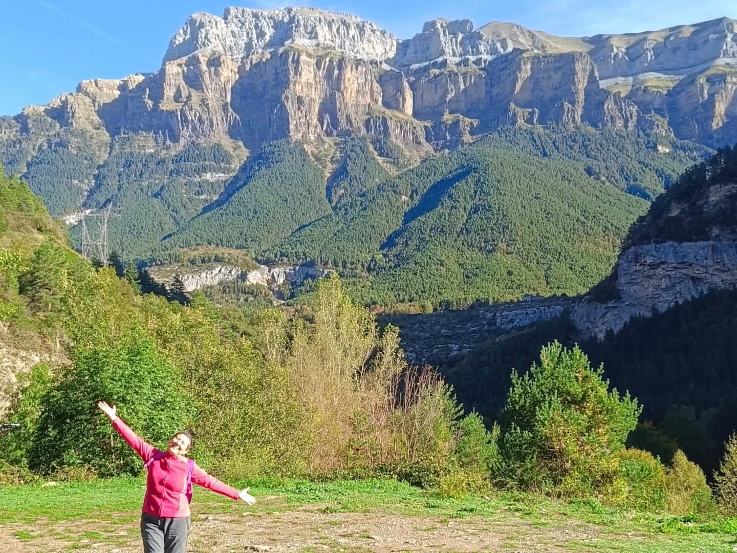 Anaís Isarre feliz con los brazos abiertos celebrando la llegada a los paisajes del Pirineo con los paredones rocosos de Ordesa de fondo.
